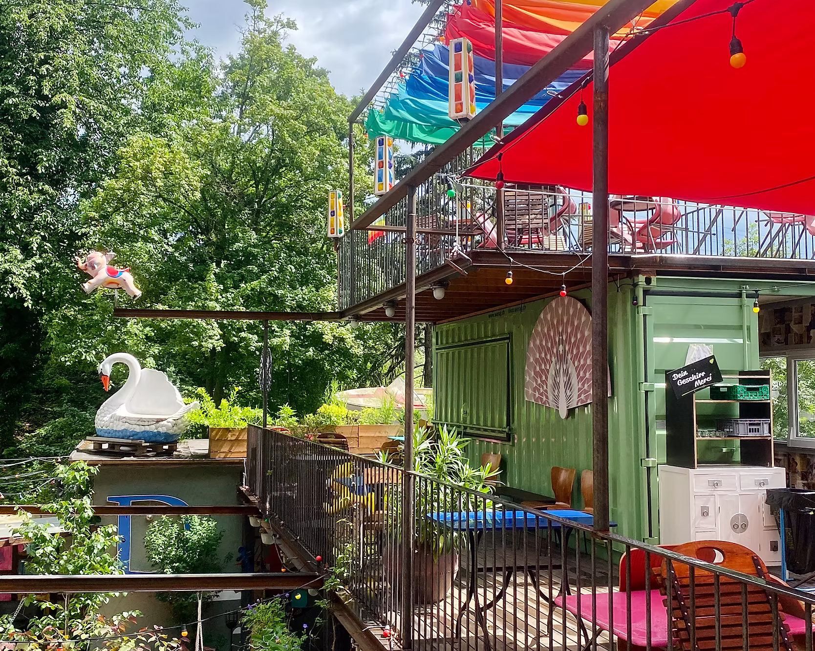 Bar am Damm garden — colourful outdoor terrace with wooden decking, rainbow canopy, and string lights by the Limmat