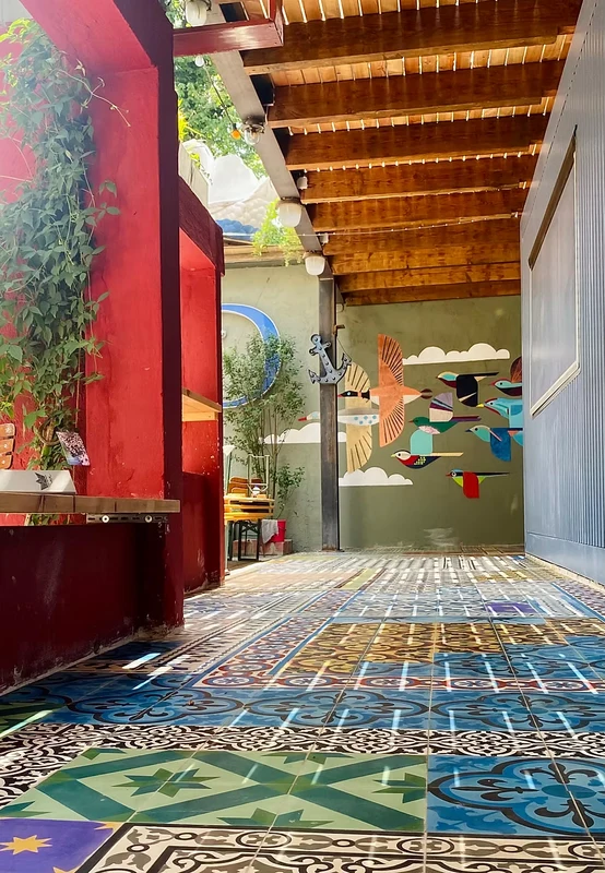 Bar am Damm covered terrace — colourful patterned tile floor under a wooden pergola with a bird mural on the back wall
