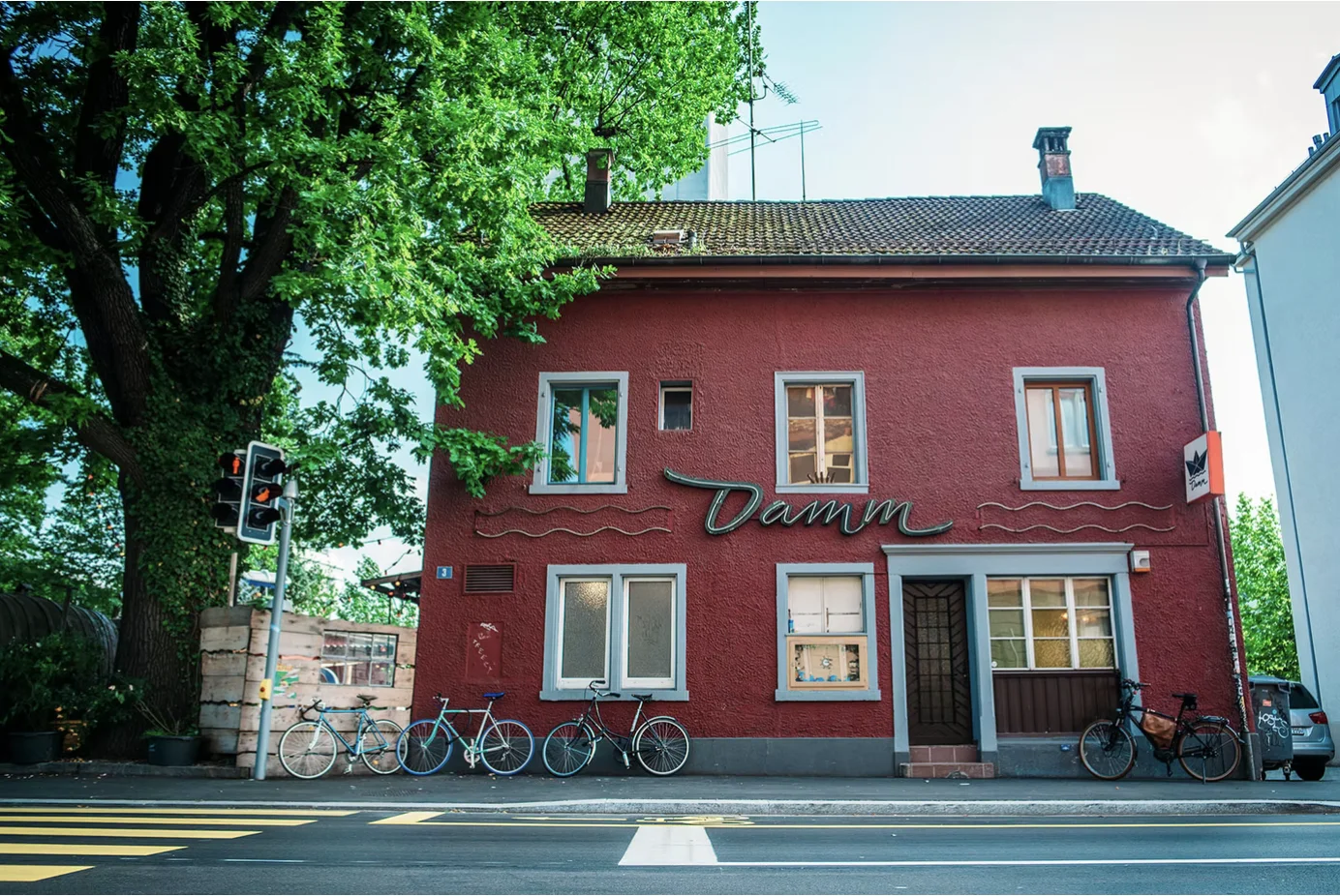 Bar am Damm exterior — terracotta building with the Damm logo on the facade, beneath a large tree